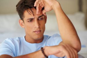 young adult male sits on bed holding his head because of prescription drug addiction symptoms