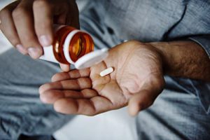 african american male pours a pill from a prescription bottle into his hand and thinks about needing an ambien addiction treatment center