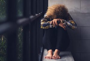 woman sits on wall by gate with her head and hands resting on her legs because of prescription drug side effects