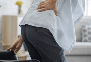 older individual gets up from chair holding back while showing signs of opiate use