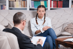 young girl sits on a couch while talking to a counselor with a clipboard in an adderall addiction treatment center