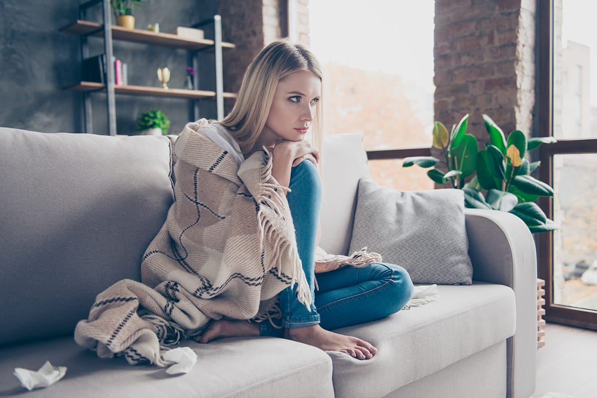 woman on couch holding blanket wondering can anxiety cause pain