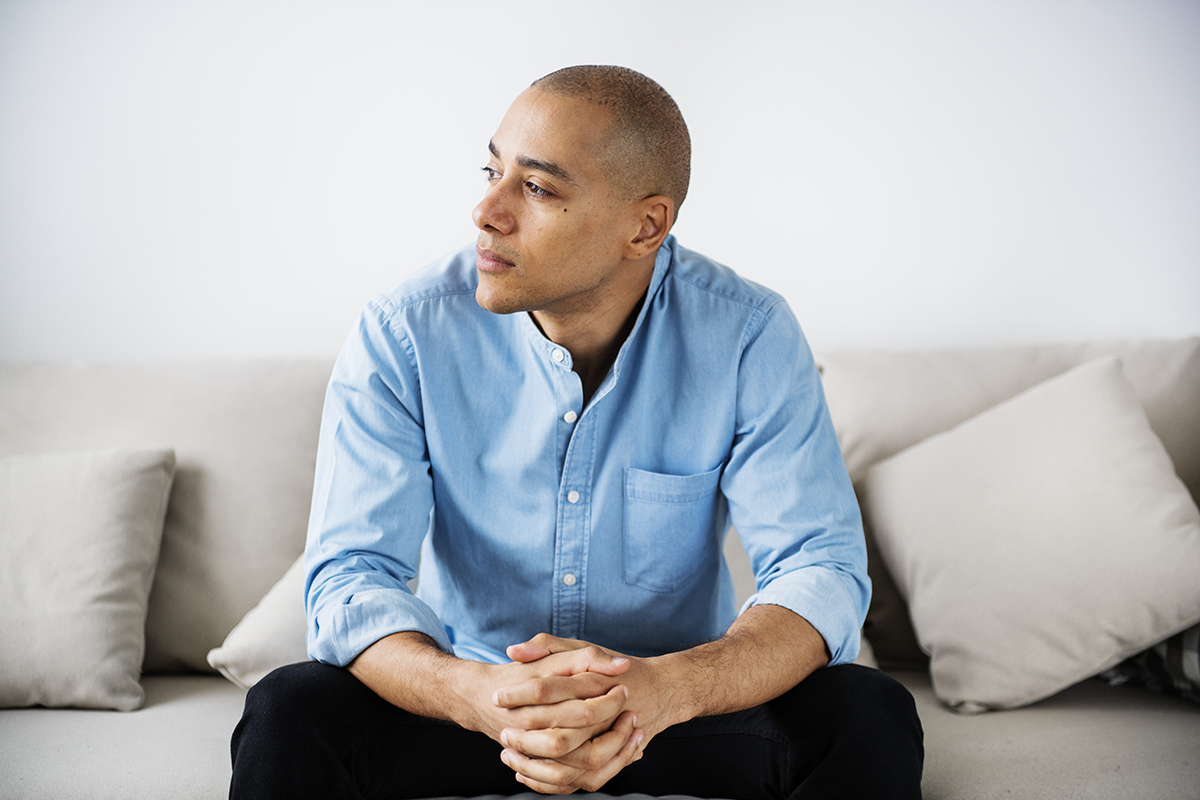 man sits on couch with his hands folded while wondering about the signs of bipolar disorder