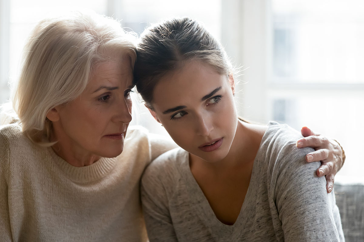 alcoholism signs, older and younger woman sitting close with their heads together forlorn