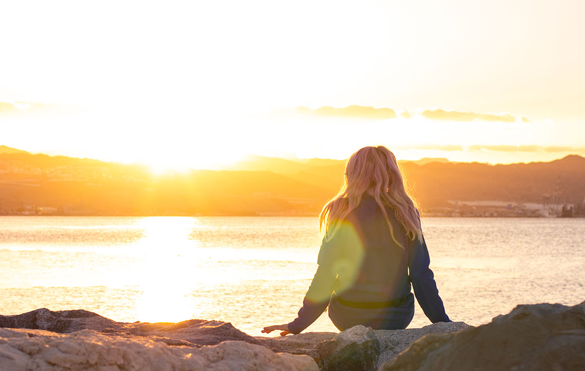 individual addiction care, woman on coast staring out over water at sunrise/sunset