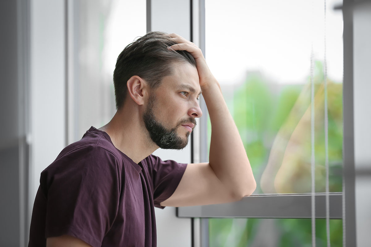 stimulant abuse, bearded man stares out window with hand propping up head