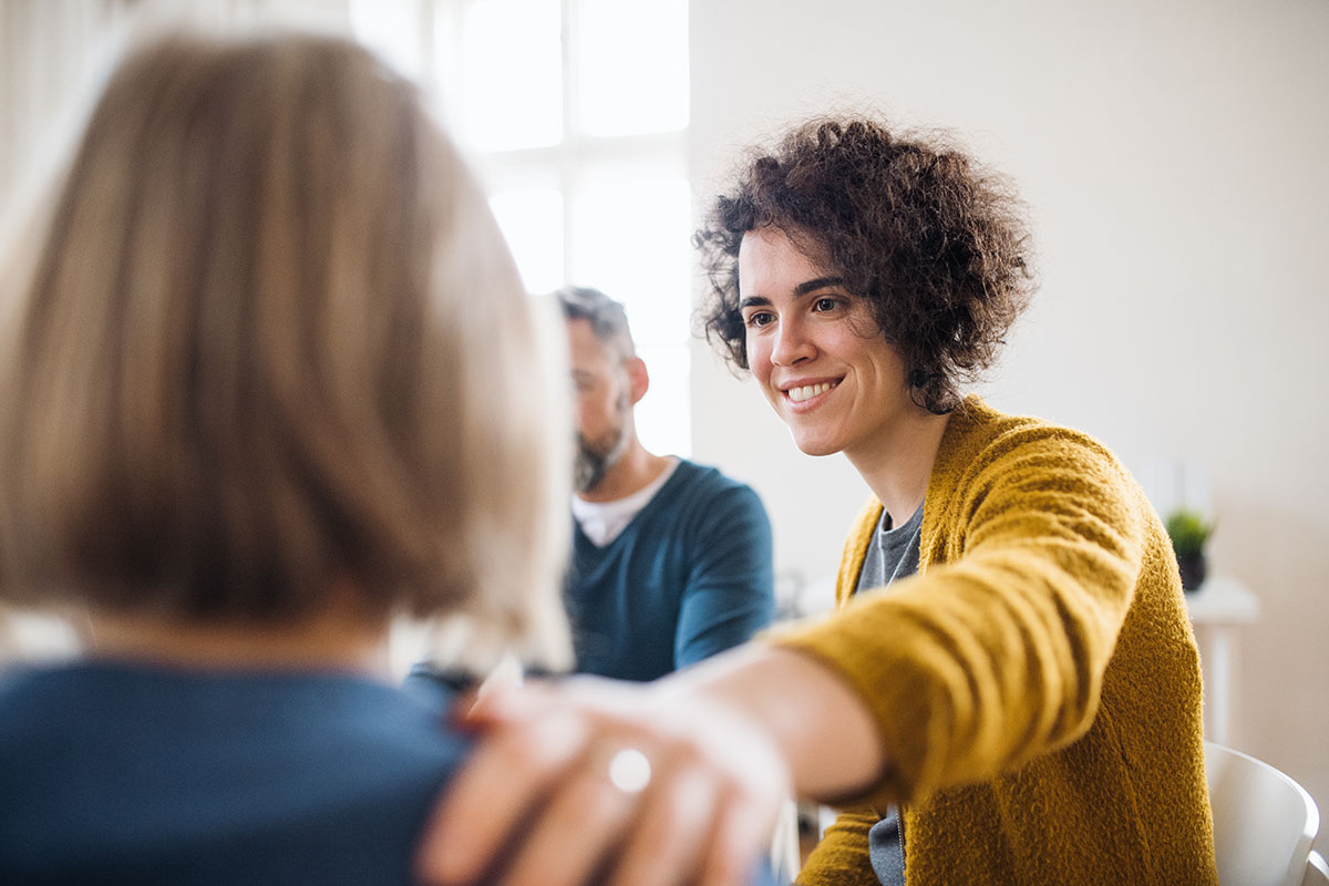 what is rehab counseling, woman smiling patting another woman on the shoulder in group therapy