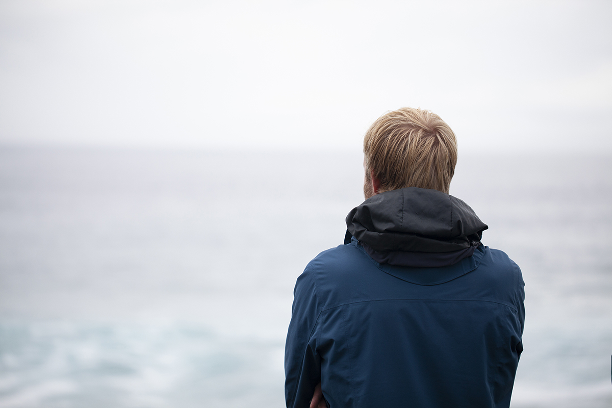 young man looking at water struggling with trauma and addiction