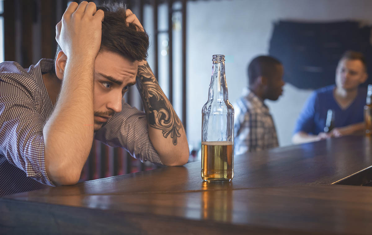 man looking at beer bottle wondering does my addiction need treatment